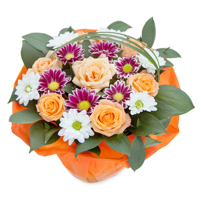 Highly detailed and lush, this bouquet is beautifully photographed from a slightly raised, overhead viewpoint, framed by a clean white surface that highlights every vibrant element. The focal point features a collection of roses opening in full splendor, their petals melting through gradients of peach, apricot, and bright orange-a celebratory nod to the welcoming spirit of Kingsbury. Amongst them are daisy-like chrysanthemums with white petals and luminous green centers, drawing a sense of freshness you might find wandering past gardens near Old Kenton Lane. Accenting the traditional touches, deep magenta and purple chrysanthemums add a rich tapestry of color that feels both festive and sophisticated-perfect for elevating an anniversary dinner or special event in the local community. The bouquet's dense green foliage, glossy and broad-leafed, adds volume and a living backdrop to the textured blooms. Thoughtfully placed, a loop of slender bright green bear grass sweeps upward, adding a refinement and lightness-a modern twist on classic floral design. Bound at the base in crinkled, vivid orange cellophane, the wrapping unites the bouquet's hues and infuses the arrangement with festive energy. This thoughtfully curated bouquet radiates joy, freshness, and the expert touch of a Kingsbury florist, making it ideal for gifting, home décor, or heralding any special occasion in the area.